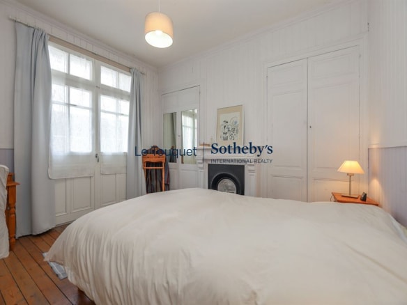 Chambre lumineuse avec lit double, fenêtres et parquet en bois.
