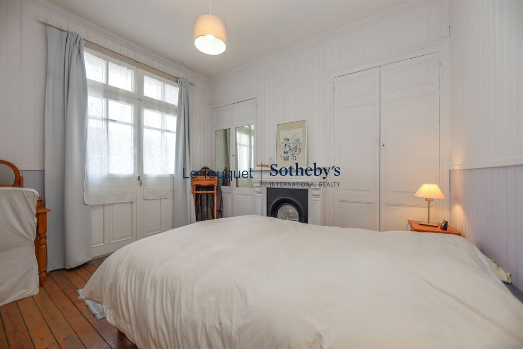Chambre lumineuse avec lit double, fenêtres et parquet en bois.