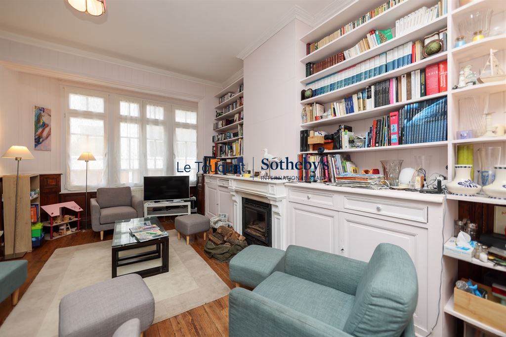 Intérieur d'une villa avec un salon lumineux, des étagères remplies de livres et un parquet en bois.