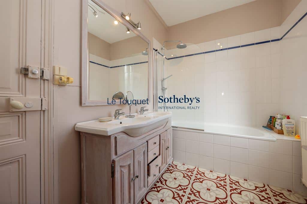 Salle de bain avec baignoire et lavabo, carrelage décoratif au sol.