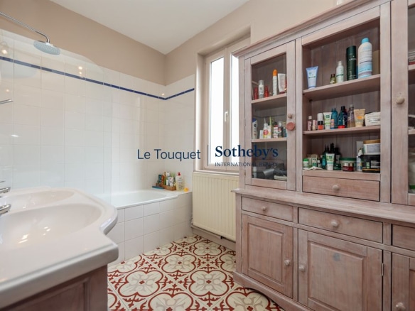 Salle de bain avec baignoire, lavabo et meuble de rangement en bois, carrelage décoratif au sol.