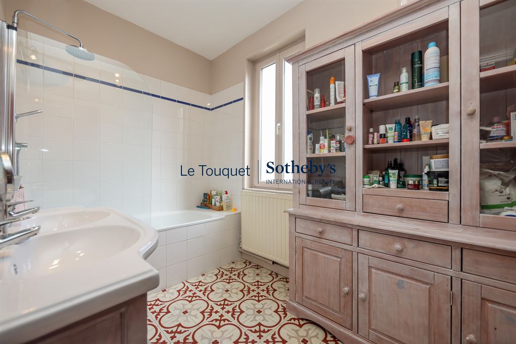 Salle de bain avec baignoire, lavabo et meuble de rangement en bois, carrelage décoratif au sol.