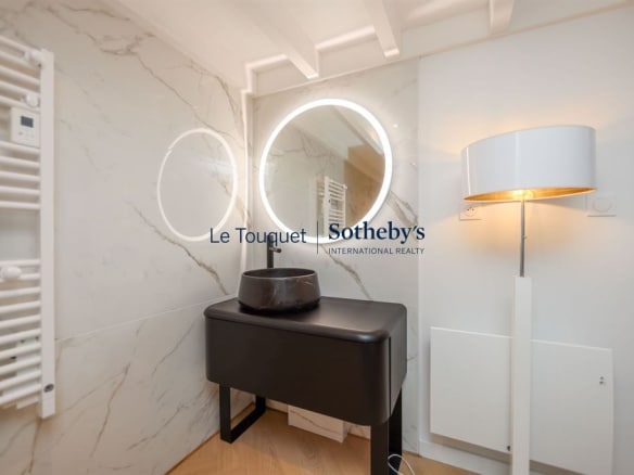 Modern bathroom with round mirror and lighting, marble and black furniture.
