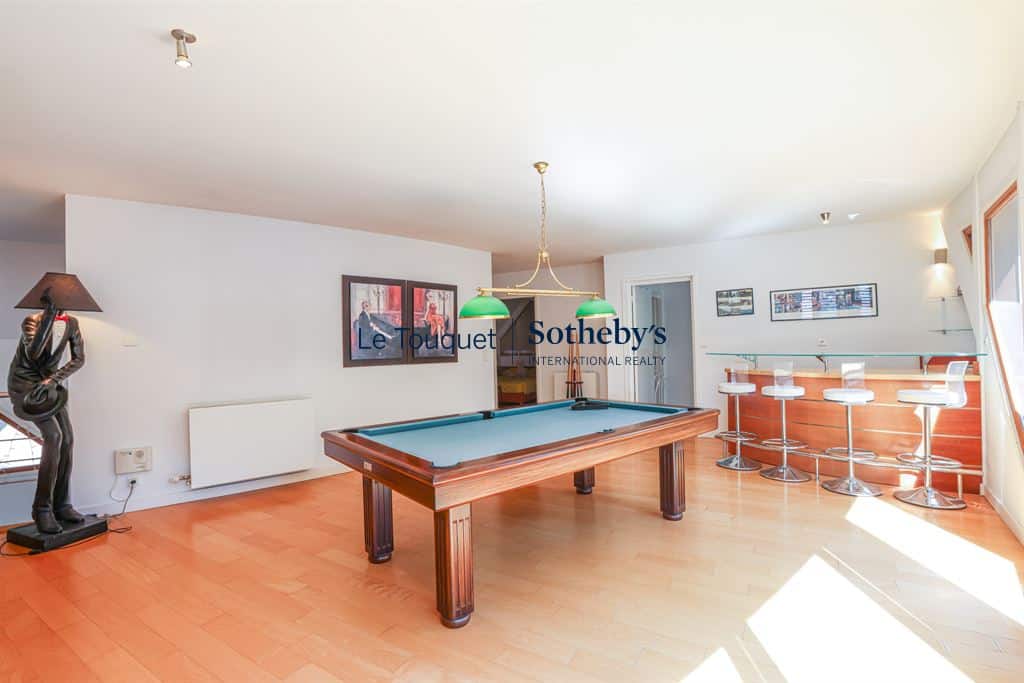 Interior of a contemporary villa with a pool table, bar and large, bright windows.
