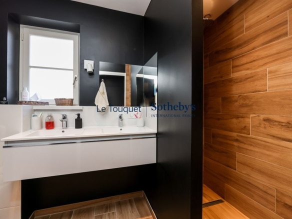 Modern bathroom with sink and shower, black and wood walls, warm lighting.