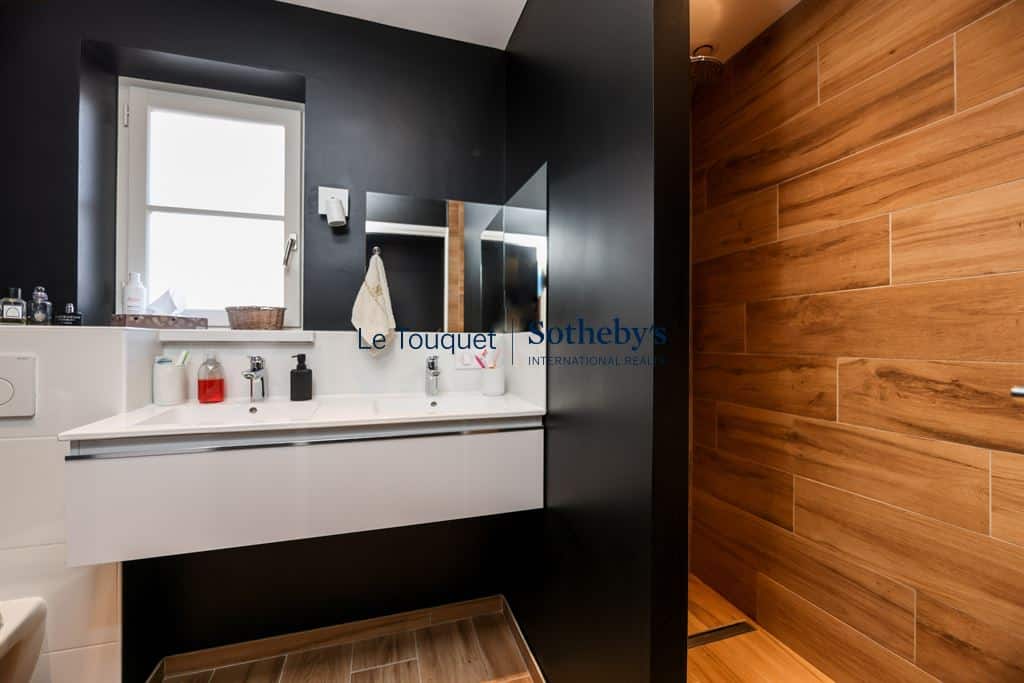 Modern bathroom with sink and shower, black and wood walls, warm lighting.