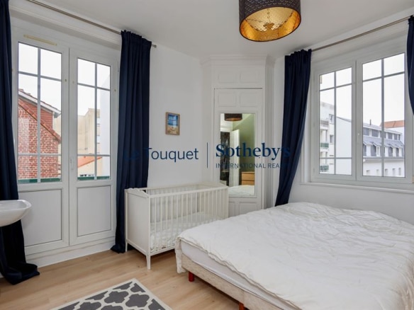 Room in a renovated apartment with bed and cot, windows overlooking the outside.