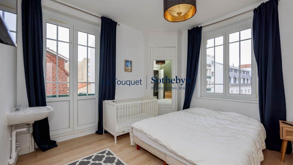 Room in a renovated apartment with bed and cot, windows overlooking the outside.