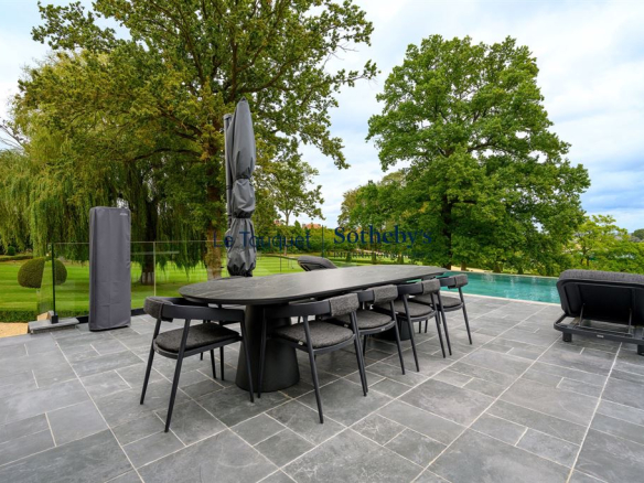 Terrasse en pierre avec mobilier moderne, vue sur un parc verdoyant et une piscine extérieure.
