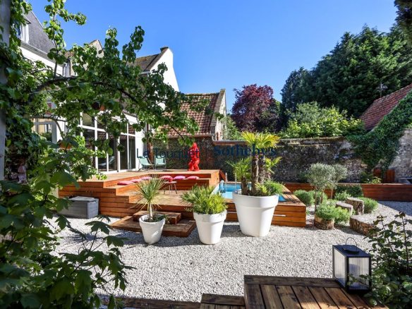 Jardin d'un hôtel particulier du XVIIIème siècle à Montreuil-sur-Mer, avec des plantes et une terrasse en bois.
