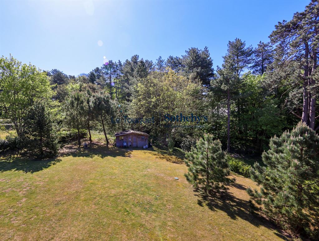 View of a garden with a wooden chalet surrounded by trees in Hardelot.