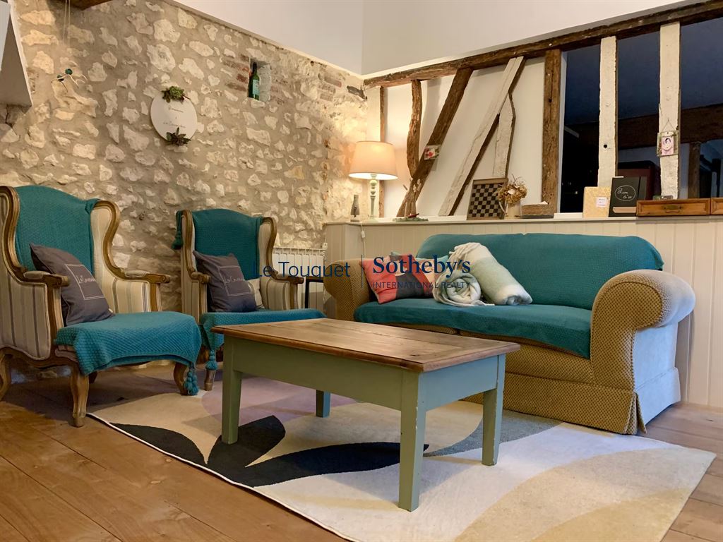 Living room of a renovated property with armchairs and a sofa, exposed stone walls.