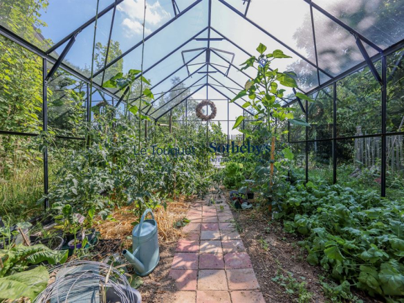 Greenhouse with plants and a paved path, located in a garden in Doudeauville.