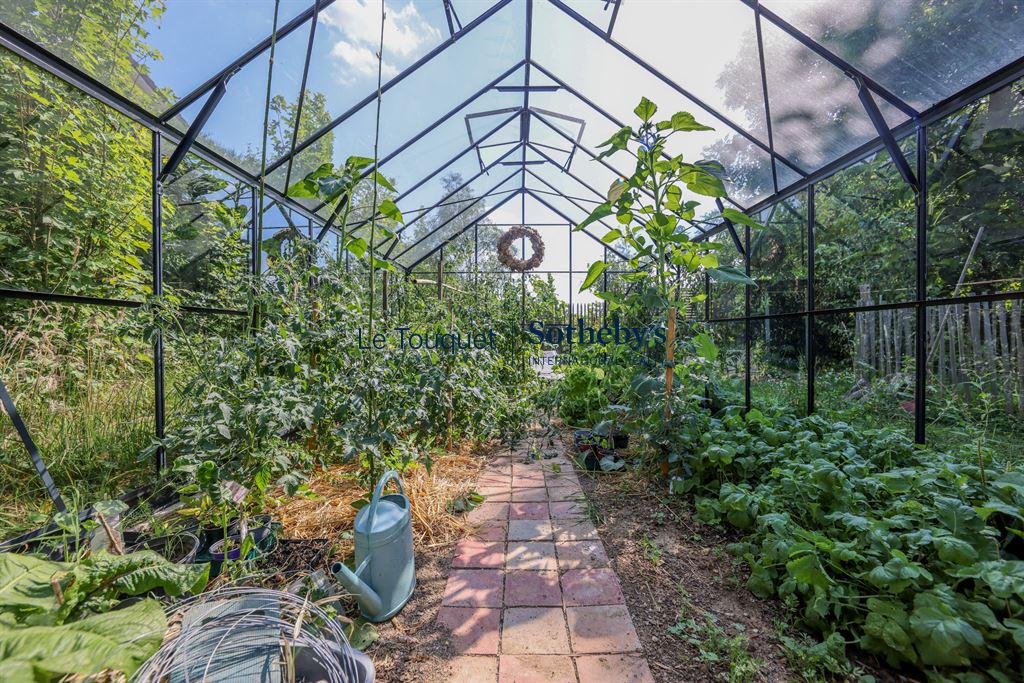Greenhouse with plants and a paved path, located in a garden in Doudeauville.