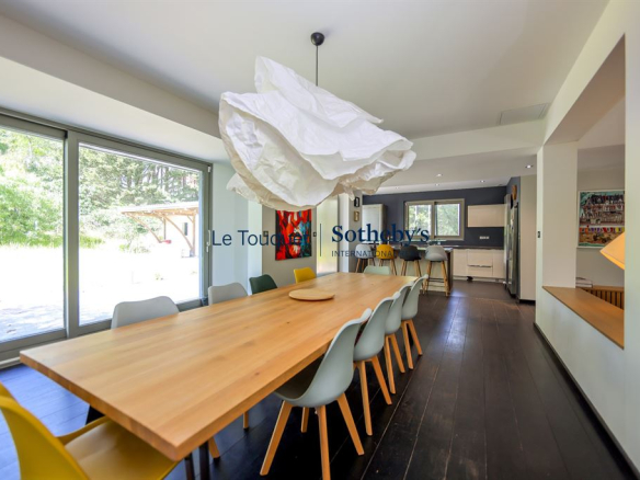 Intérieur d'une villa contemporaine avec salle à manger et cuisine ouverte, grandes baies vitrées donnant sur le jardin.