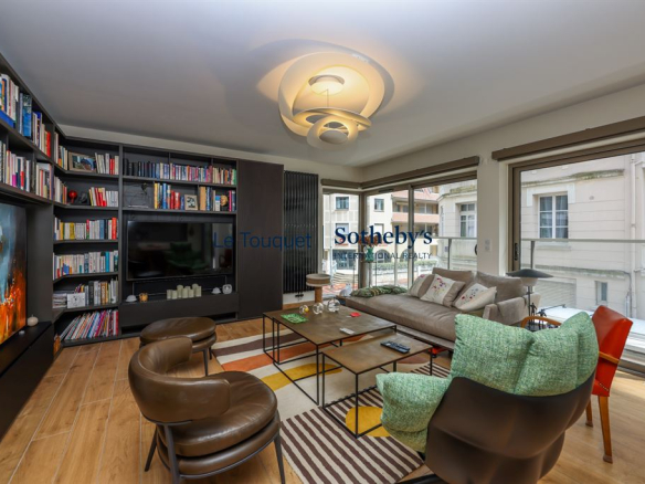 Salon lumineux d'un appartement moderne avec canapé, bibliothèque et terrasse au Touquet-Paris-Plage.