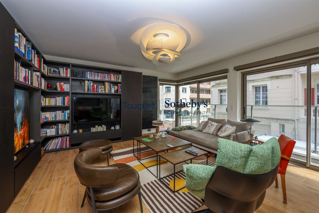 Salon d’un appartement au Touquet-Paris-Plage Salon lumineux d'un appartement moderne avec canapé, bibliothèque et terrasse au Touquet-Paris-Plage.