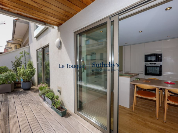 Terrasse d'un appartement moderne avec vue sur une pièce de vie lumineuse et cuisine équipée.
