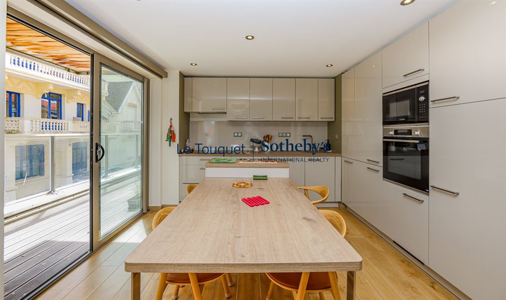 Cuisine d’un appartement au Touquet-Paris-Plage Cuisine moderne d'un appartement avec table en bois et accès à une terrasse.