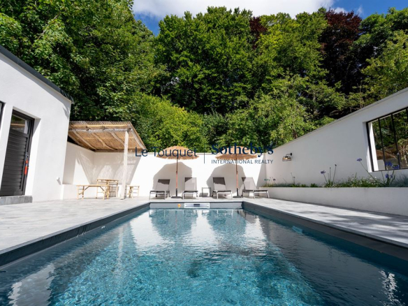 Swimming pool surrounded by sun loungers and white walls, with trees in the background.