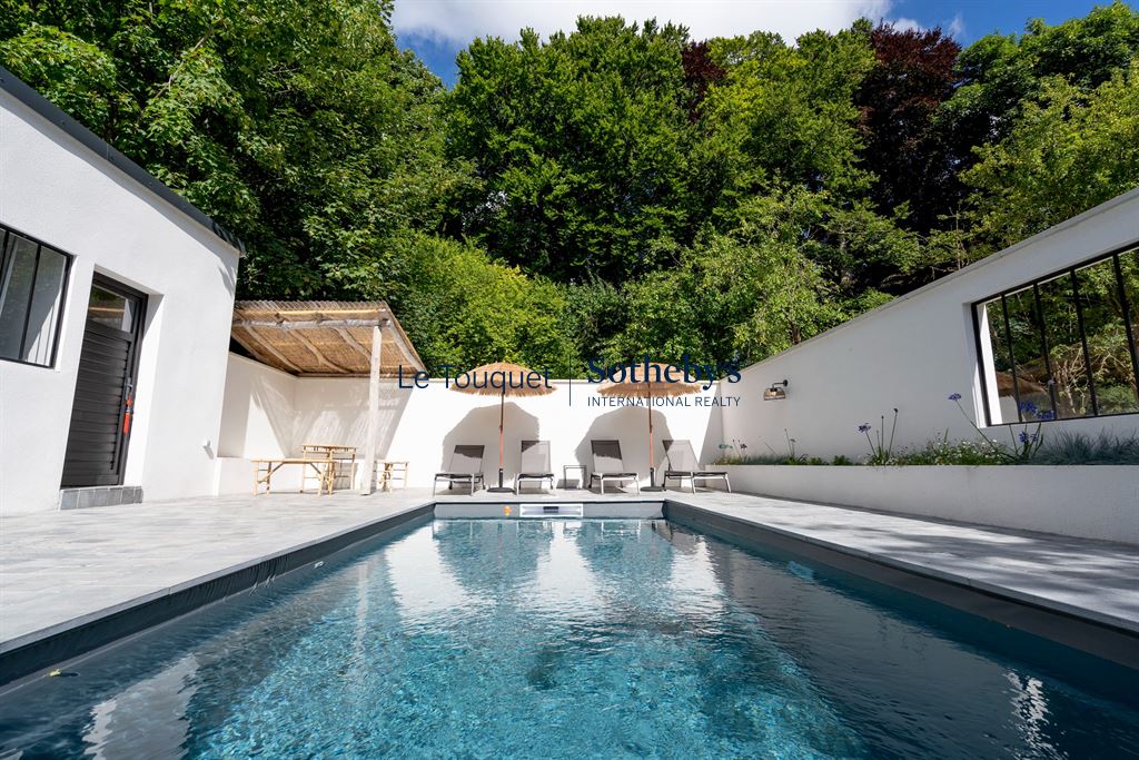 Swimming pool surrounded by sun loungers and white walls, with trees in the background.
