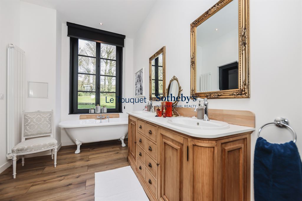 Modern bathroom with bathtub, wooden vanity and gilded mirror, natural light